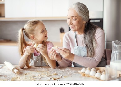 Smiling Old Grandmother In Apron Teaching Little Granddaughter Making Dough, Mold Cookies, Prepare Food In Minimalist Kitchen Interior. Household Chores Together, Cooking Lesson At Home, Free Space