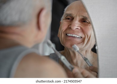 Smiling old man brushing his teeth prosthesis with toothbrush. Odontic healthcare concept. - Shutterstock ID 2174503547