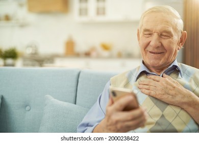 Smiling Old Man Looking At Phone Screen At Home