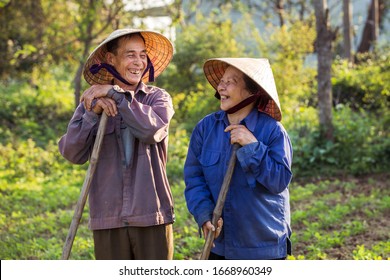 Smiling old Vietnamese couple on a farm with conical hats (non la)