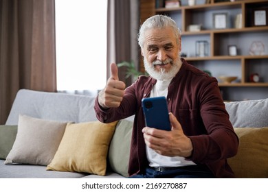 Smiling Older Man Sitting On Couch Giving Thumb Up While Playing Computer Game, Looking At Camera, Smiling.