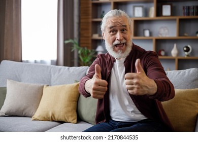 Smiling Older Man Sitting On Couch Giving Thumb Up While Playing Computer Game, Looking At Camera, Smiling.