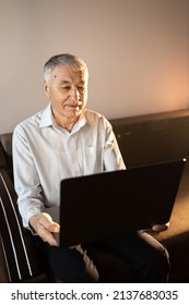 Smiling Older Man Using Laptop At Home, Looking At Screen, Searching Information In Internet, Happy Mature Male Making Video Call, Sitting On Couch. 