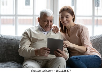 Smiling older mature male retiree showing funny photos on digital computer tablet to affectionate caring grown daughter, relaxing together on couch indoors, different generations hobby pastime. - Powered by Shutterstock