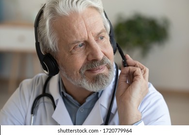 Smiling older senior physician wearing headset with microphone looking away. Online doctor consultation, tele medicine and remote medical assistance, telehealth distance services concept. Close up.