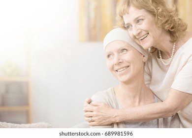 Smiling Older Woman Hugging Her Friend With Cancer Wearing A Scarf