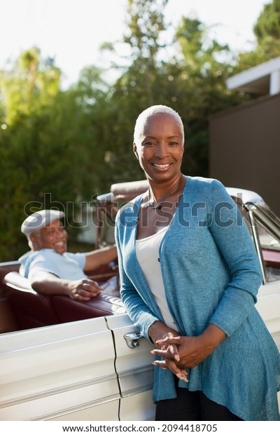 Smiling older woman\
leaning on convertible