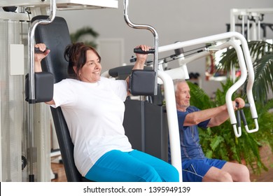 Smiling older woman working out at gym. Pretty positive woman flexing muscles using machine at fitness center. Fitness, sport, training, people and lifestyle concept.