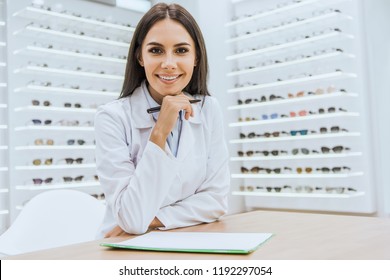 Smiling Optician With Papers And Pen Looking At Camera In Ophthalmology