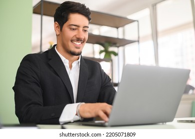 Smiling optimistic young latin entrepreneur wearing smart casual clothes, sitting at the desk, typing on keyboard, businessman professional is feeling ready to work and start new projects - Shutterstock ID 2205071809