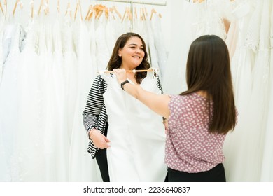 Smiling overweight woman looking excited shopping for a wedding dress with the help of a friend - Powered by Shutterstock