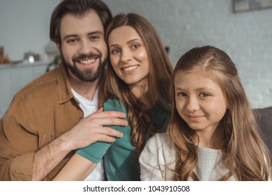 smiling parents and daughter looking at camera at home - Shutterstock ID 1043910508