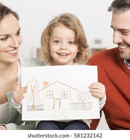 Smiling parents and their kid are sitting in the living room  A boy is holding drawing house