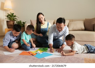 Smiling parents   their three sons drawing pictures floor together