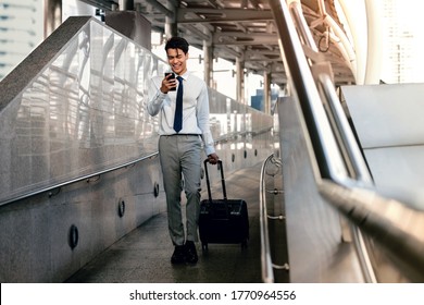 Smiling  Passenger Businessman Using Mobile Phone while Walking with Suitcase in the Airport or Public Transportation Station. Lifestyle of Modern People. Full Length