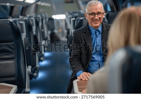 Smiling passenger having a friendly conversation with a fellow traveler while journeying on a comfortable, modern train, highlighting connection and relaxation during transit