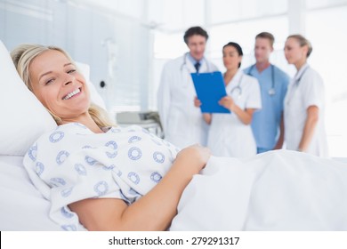 Smiling patient looking at camera with doctors behind in hospital room - Powered by Shutterstock