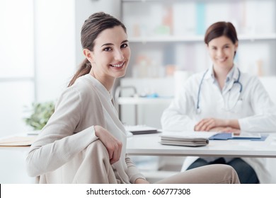 Smiling patient receiving a medical consultation and looking at camera, the female doctor is sitting at desk on the background