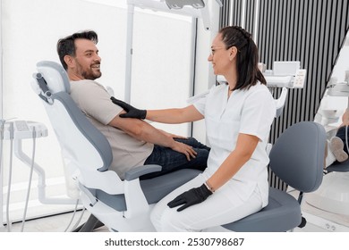 Smiling patient sitting in a dental chair while talking to a dentist in a modern clinic - Powered by Shutterstock