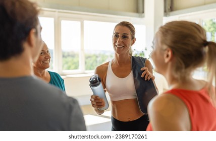 Smiling people chatting in a gym with a woman holding a water bottle in the foreground. Teamwork Concept image - Powered by Shutterstock