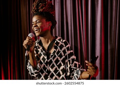 Smiling performer holding microphone while performing on stage. Vibrant energy and joy radiating from the performance as the crowd engages with the act