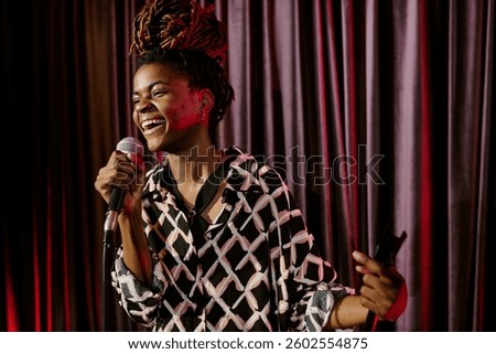 Smiling performer holding microphone while performing on stage. Vibrant energy and joy radiating from the performance as the crowd engages with the act