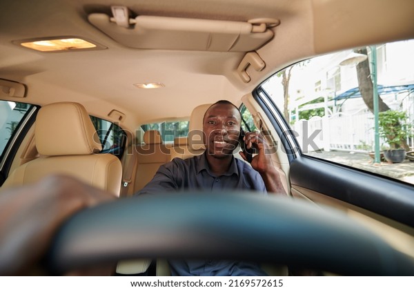 Smiling personal driver talking on phone with client\
when driving car