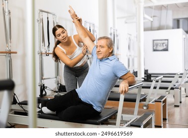 Smiling personal female trainer assisting mature man exercising on Pilates machine in rehabilitation center - Powered by Shutterstock