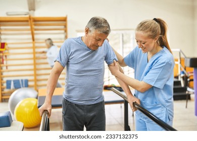 Smiling physiotherapist assisting elderly man in movement therapy at rehabilitation center - Powered by Shutterstock