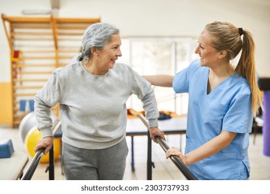 Smiling physiotherapist assisting happy senior woman to walk during movement therapy at rehab center - Powered by Shutterstock