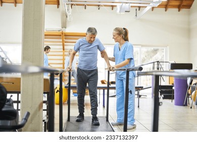 Smiling physiotherapist assisting senior man to walk during movement therapy at rehabilitation center