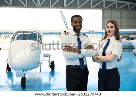Smiling pilot students posing with arms crossed in aircraft hangar