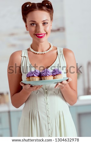 Smiling pin up girl holding plate of cupcakes and looking at camera