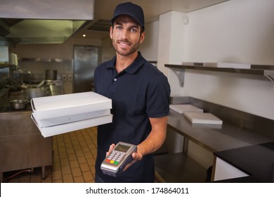 Smiling pizza delivery man holding credit card machine in a commercial kitchen - Powered by Shutterstock