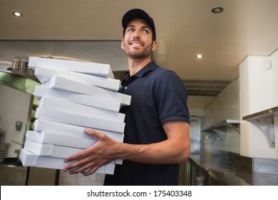Smiling pizza delivery man holding many pizza boxes in a commercial kitchen