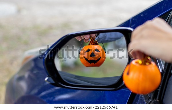 smiling plastic halloween pumpkin mini small pumpkin\
in reflection rear view retractable lateral mirror.woman hand\
holding pumpkin bucket handle.trick or treat holiday, car auto\
vehicle vehicle part