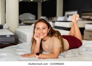 Smiling pleasant cheerful positive Hispanic girl lying on new modern orthopedic mattress in furniture shop trying its comfort and convenience
