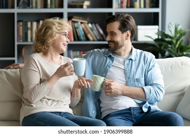 Smiling pleasant middle aged senior mother chatting with grown up son, relaxing together on comfortable sofa with cups of tea in hands, sharing life news, gossiping or joking on weekend at home. - Powered by Shutterstock