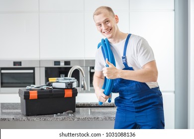 Smiling plumber giving a thumbs-up to a customer standing next a tool box in a kitchen - Powered by Shutterstock