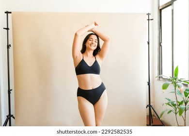 Smiling plus size woman in black underwear with her arms above her head feeling a lot of self love embracing body positivity
