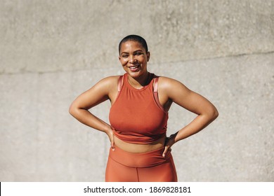 Smiling plus size woman sportswear standing with her hands on hips after workout. Healthy woman relaxing after physical training session outdoors.