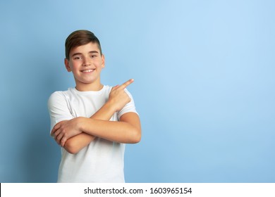 Smiling, pointing at side. Caucasian boy portrait isolated on blue studio background. Beautiful teen male model in white shirt posing. Concept of human emotions, facial expression, sales, ad. - Shutterstock ID 1603965154