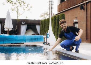 Smiling pool maintenance worker checking water quality by touching the surface of a swimming pool in a luxury hotel resort