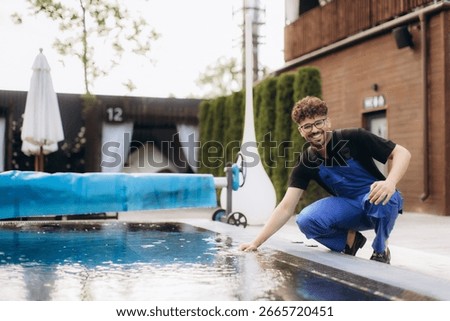 Smiling pool maintenance worker checking water quality by touching the surface of a swimming pool in a luxury hotel resort