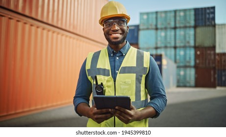 Smiling Portrait of a Handsome African American Black Industrial Engineer in Yellow Hard Hat and Safety Vest Working on Tablet Computer. Foreman or Supervisor in Container Terminal. - Powered by Shutterstock