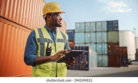 Smiling Portrait of a Handsome African American Black Industrial Engineer in Yellow Hard Hat and Safety Vest Working on Tablet Computer. Foreman or Supervisor in Container Terminal. - Powered by Shutterstock