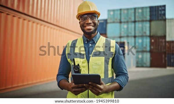 Smiling\
Portrait of a Handsome African American Black Industrial Engineer\
in Yellow Hard Hat and Safety Vest Working on Tablet Computer.\
Foreman or Supervisor in Container\
Terminal.