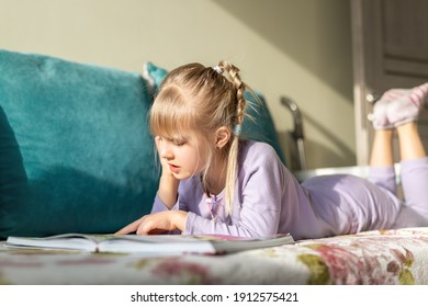 Smiling portrait little cute adorable happy blond caucasian kid girl enjoy lying on sofa bed and reading fairy tale story book. Small female child person reading, dreaming and imagination development - Powered by Shutterstock