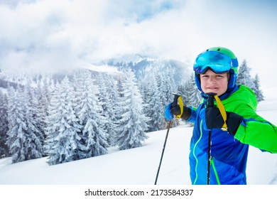 Smiling Portrait Of A Young Boy Hold Poles Wearing Ski Helmet And Mask Smile Standing Over Forest After Heavy Snowfall