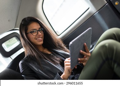 Smiling Portrait Of Young Mixed Race Businesswoman Inside A Taxi In Canary Wharf Area In London While Using A Tablet.